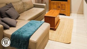 Una sala de estar con un sofá color beige, una mesa de centro de madera, un televisor de pantalla plana sobre un mueble de madera y un elemento decorativo en la pared.