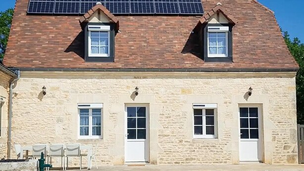 Un edificio de piedra con techo de tejas, tres ventanas y un panel solar.