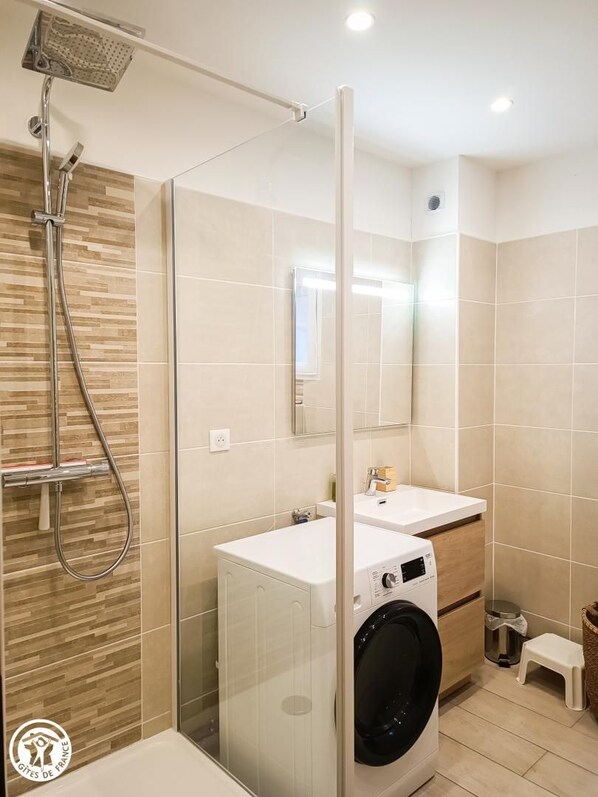 A modern bathroom with a glass shower enclosure, a built-in washing machine, and a small stool.