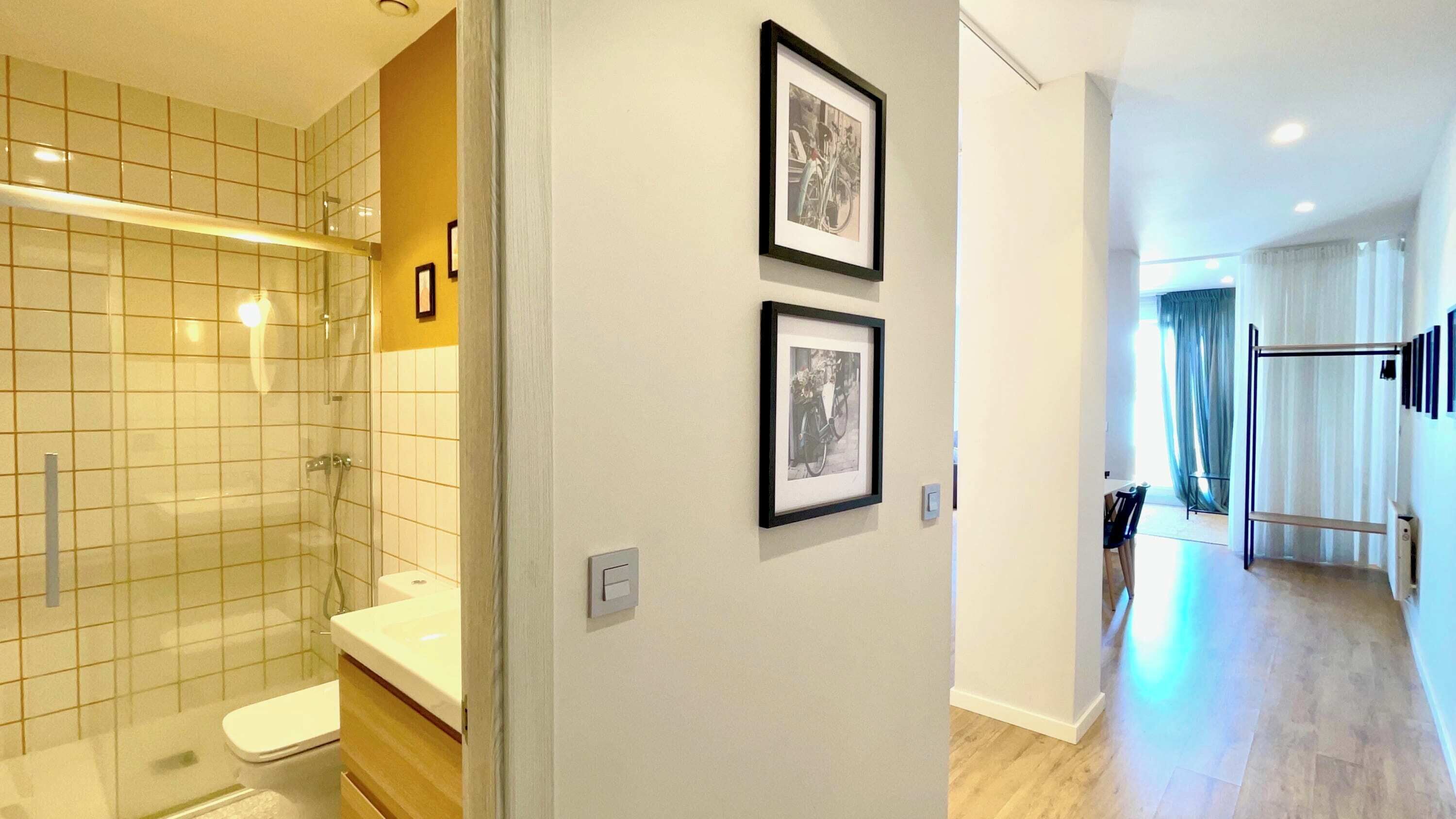 A modern bathroom with a glass shower enclosure, a toilet, and a sink. There are two framed pictures on the wall.