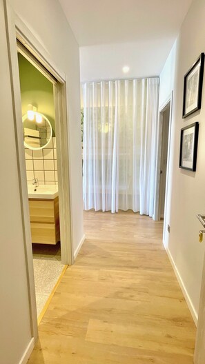 A hallway with a wooden floor, a bathroom with a mirror and sink, and white curtains. - The Cliffs A Ribeira - Rapadoira (Foz)