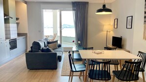 Moderni olohuone, jossa on sohva, ruokapöytä, tuoleja, televisio ja keittiöalue.