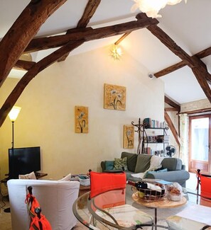 Un salón acogedor con vigas de madera a la vista, una mesa de vidrio y una estantería.