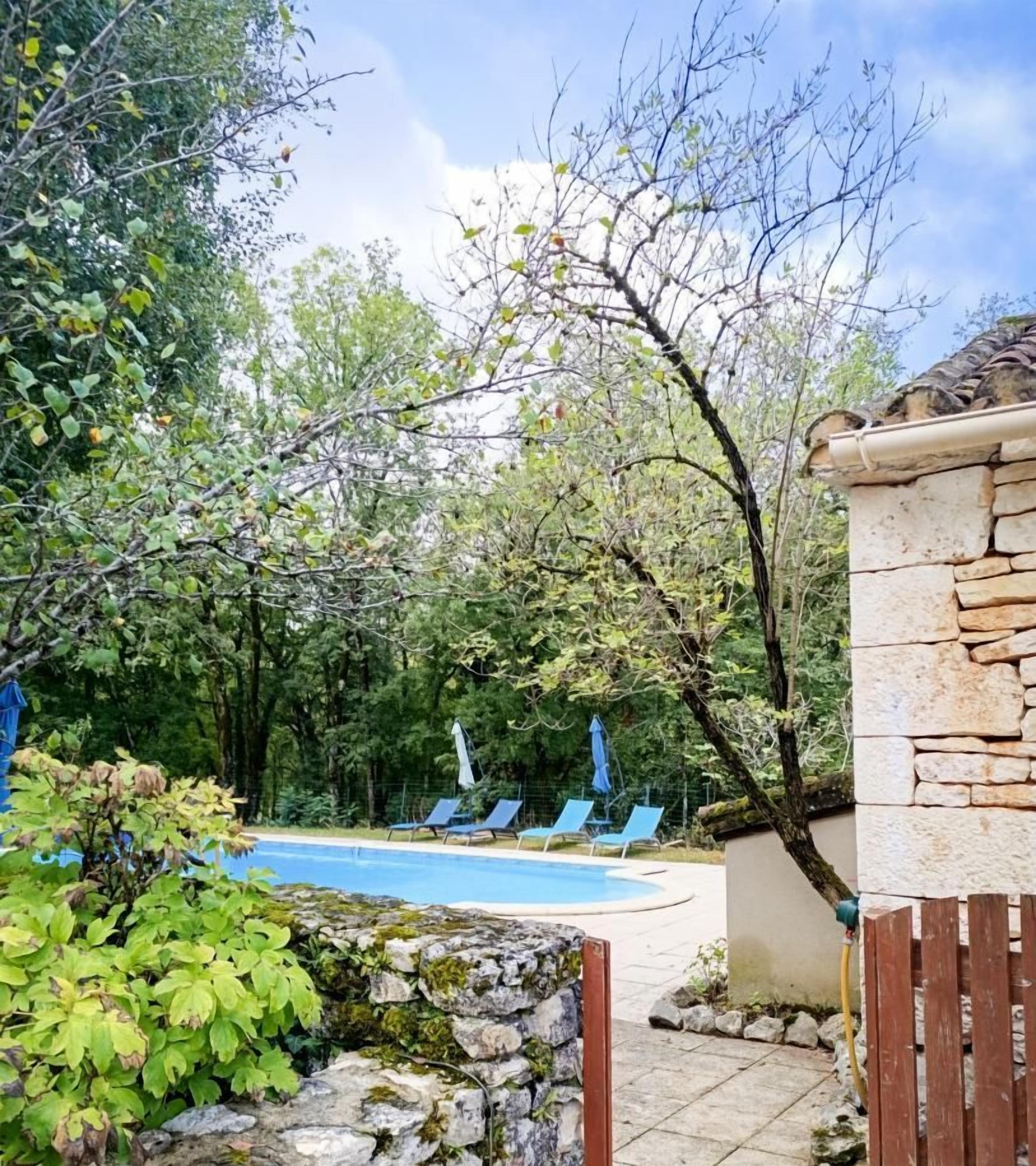 A stone wall with a pool and lounge chairs in the background.