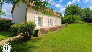 A two-story house with a red-tiled roof, white shutters, and a well-maintained lawn.