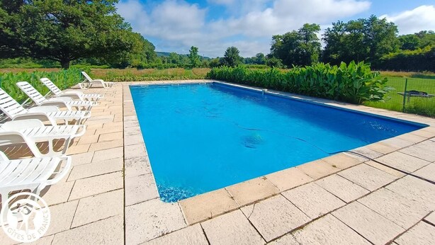 A rectangular swimming pool with clear blue water, surrounded by a paved deck.