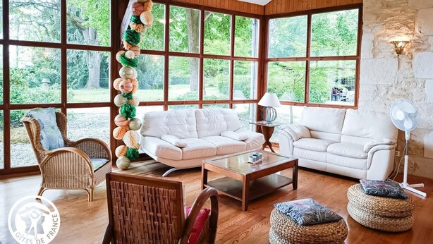 Un salón amplio con ventanas grandes, un sofá blanco, sillones de mimbre y un muro decorativo.