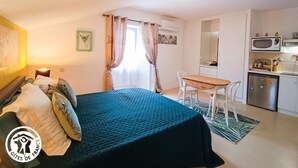 Habitación compacta con cama, una mesita, kitchenette y ventana con cortinas.