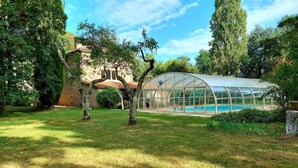 Un invernadero con piscina, rodeado de árboles y un césped.