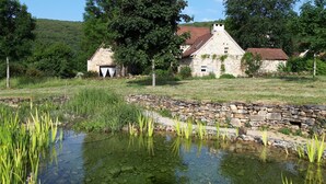 A stone house with a tiled roof, surrounded by a stone wall and a small pond with water plants. - Gîtes de France® - Le Hameau du Quercy - Stone spirit (FRONTENAC)