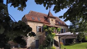A stone house with a tiled roof, a staircase leading to the entrance, and outdoor seating. - Gîtes de France® - Gîte du Tilleul (FAYCELLES)