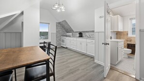 A modern kitchen with white cabinets, a wooden dining table, and a black chair. - Cozy Studio with reading nook (White Plains)