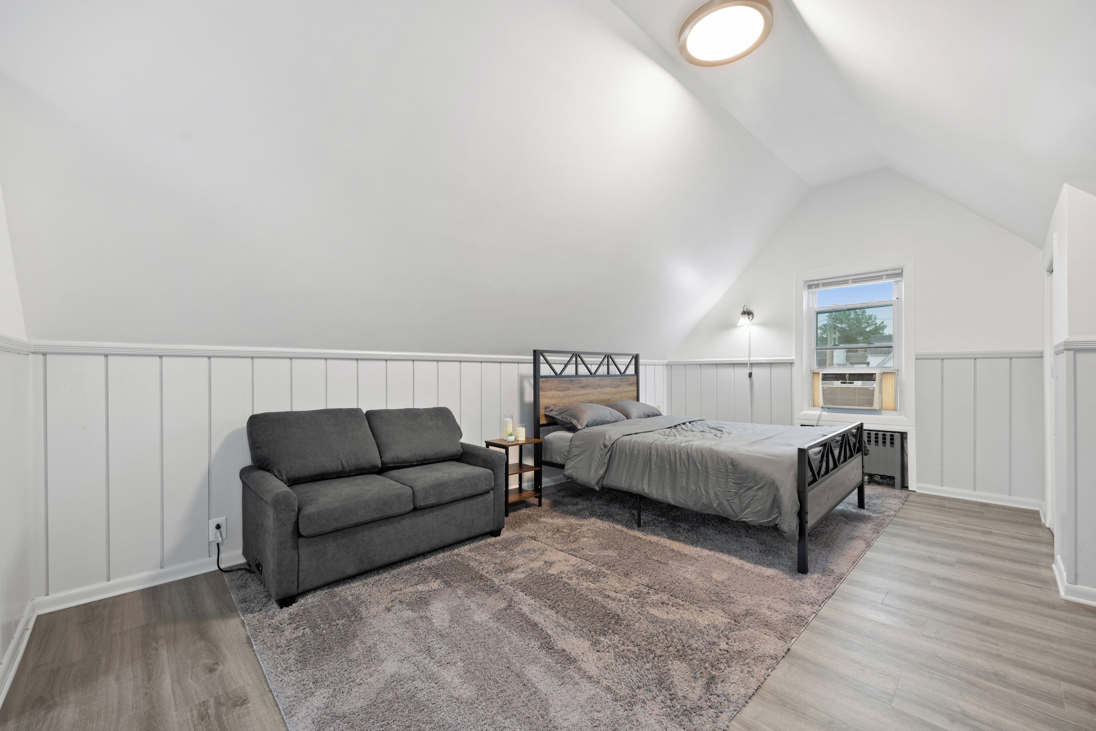 Ein Schlafzimmer mit einem Bett, einer Couch, einem kleinen Tisch und einem Fenster.