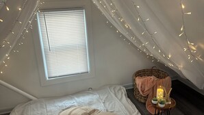 A cozy attic bedroom with a bed, pillows, a small table with candles, and string lights. - Cozy Studio with reading nook (White Plains)
