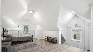 A spacious attic bedroom with a sloped ceiling, a bed, a desk, and a window. - Cozy Studio with reading nook (White Plains)
