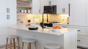 Een moderne keuken met witte kasten, een centraal eiland met krukken, een magnetron en een spoelbak.