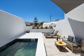 A rooftop terrace with a swimming pool, lounge chairs, a sofa, and a table with a bottle and fruit. - Terra Vecchia Suites (Santorini)