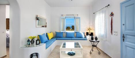 Een moderne woonkamer met een blauwe bank, een glazen salontafel en uitzicht op zee door een raam.