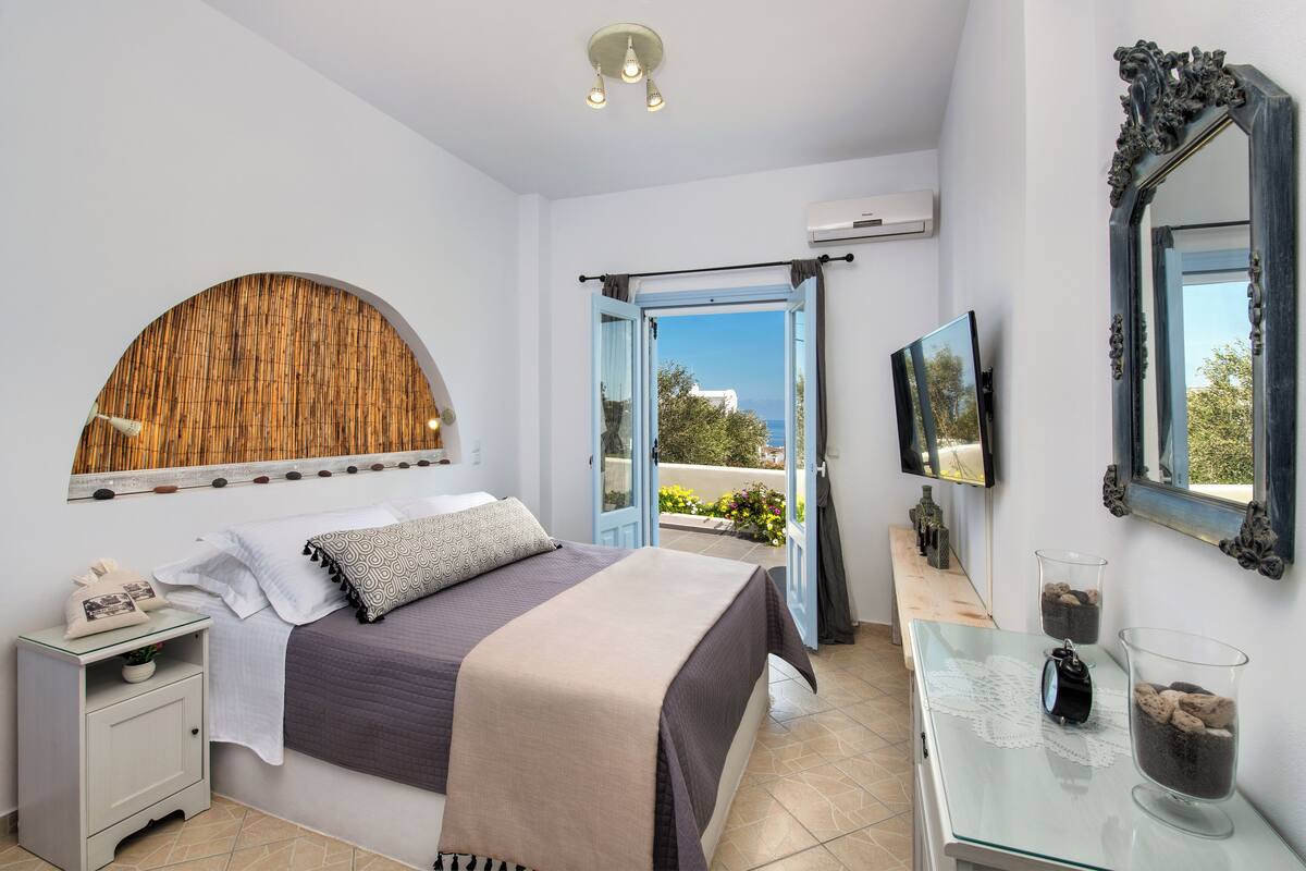 A bedroom with a bed, bedside table, and a view of the outdoors.