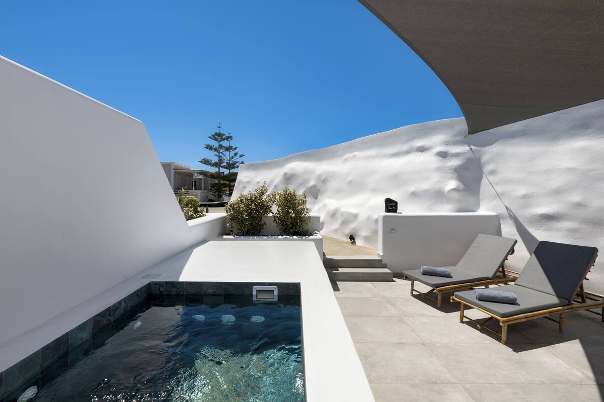 A modern outdoor pool area with a clear blue sky, a small pool, and two lounge chairs with towels.