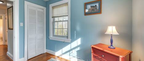 A room with blue walls, a wooden floor, a white door, a window with blinds, a red dresser, and a blue rug.