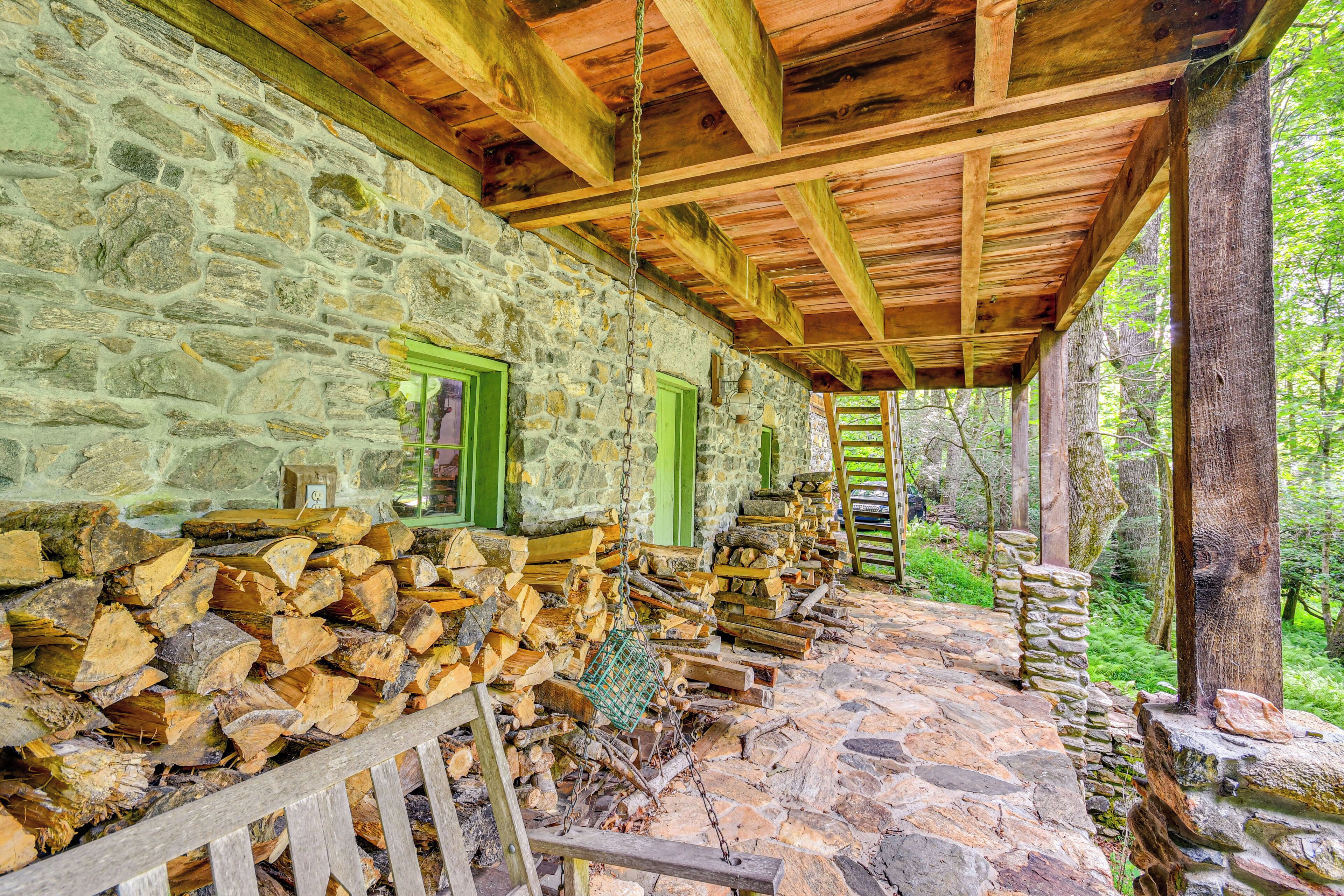 Un bâtiment rustique en pierre, doté d’un plafond en bois et d’un sol en pierre, entouré de verdure.