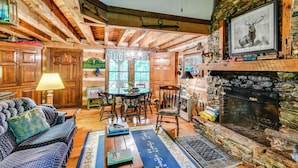 Un intérieur de chalet chaleureux avec une cheminée en pierre, des poutres en bois, un coin repas et un canapé.