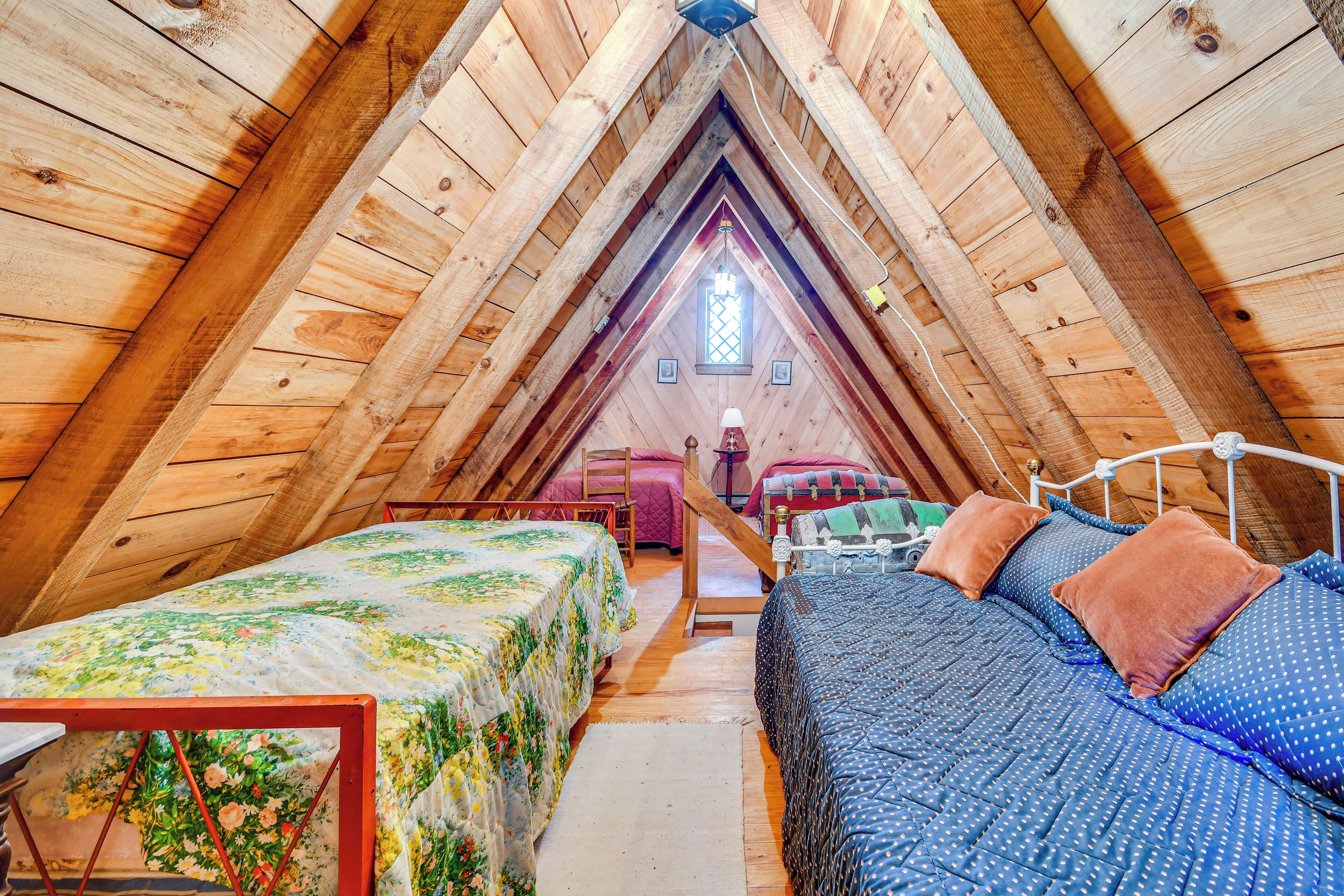 A cozy attic bedroom with two beds, wooden beams, a small window, and a wooden ceiling.