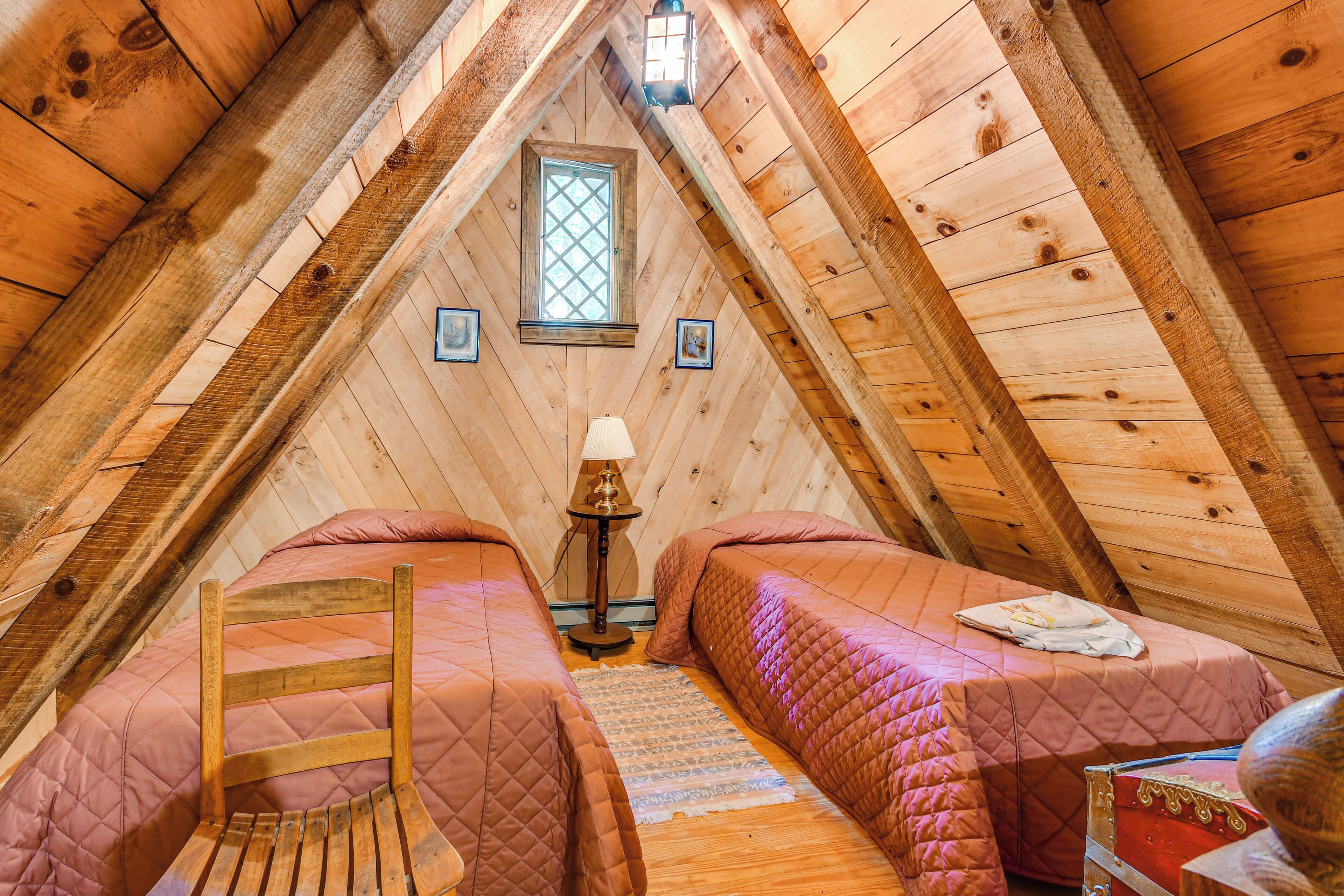 Un dormitorio cálido en el ático, con paredes de madera, una ventana, dos camas, una silla y una lámpara.
