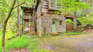 Une cabane rustique en pierre, avec une porte verte, un escalier en bois et un petit porche.