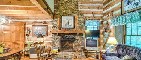 A cozy log cabin interior with a stone fireplace, wooden furniture, and a television.