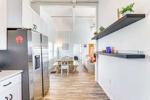 Una cocina moderna con refrigerador de acero inoxidable, suelo de madera y un comedor con mesa y sillas.