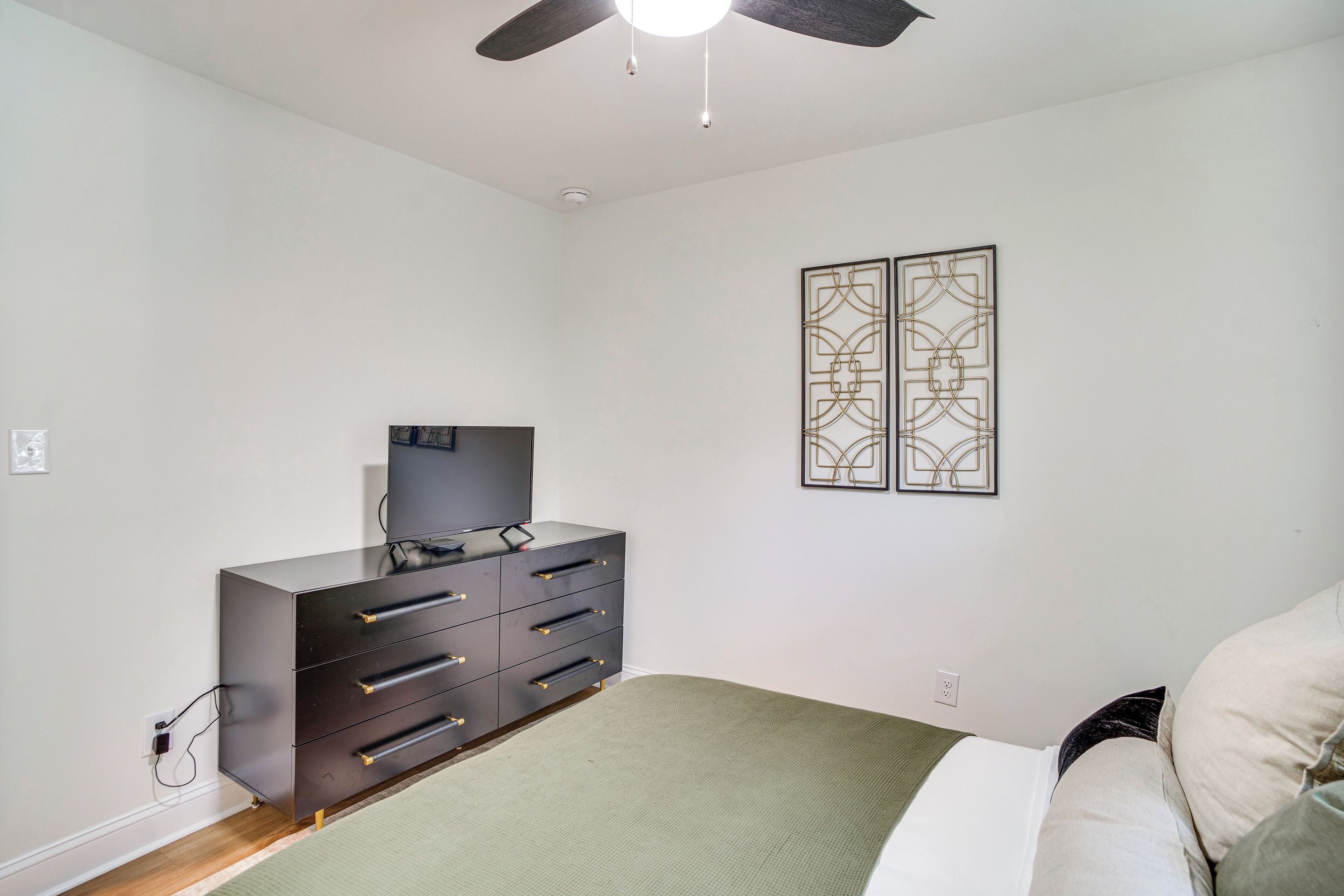 Ein Schlafzimmer mit Bett, Schminktisch, Deckenventilator und zwei Wandbildern.
