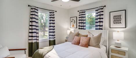 A bedroom with a bed, bedside table, lamp, and curtains.