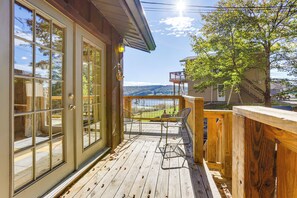 Une terrasse en bois offrant une vue sur un lac et des montagnes, un patio couvert avec des chaises et une clôture en bois.