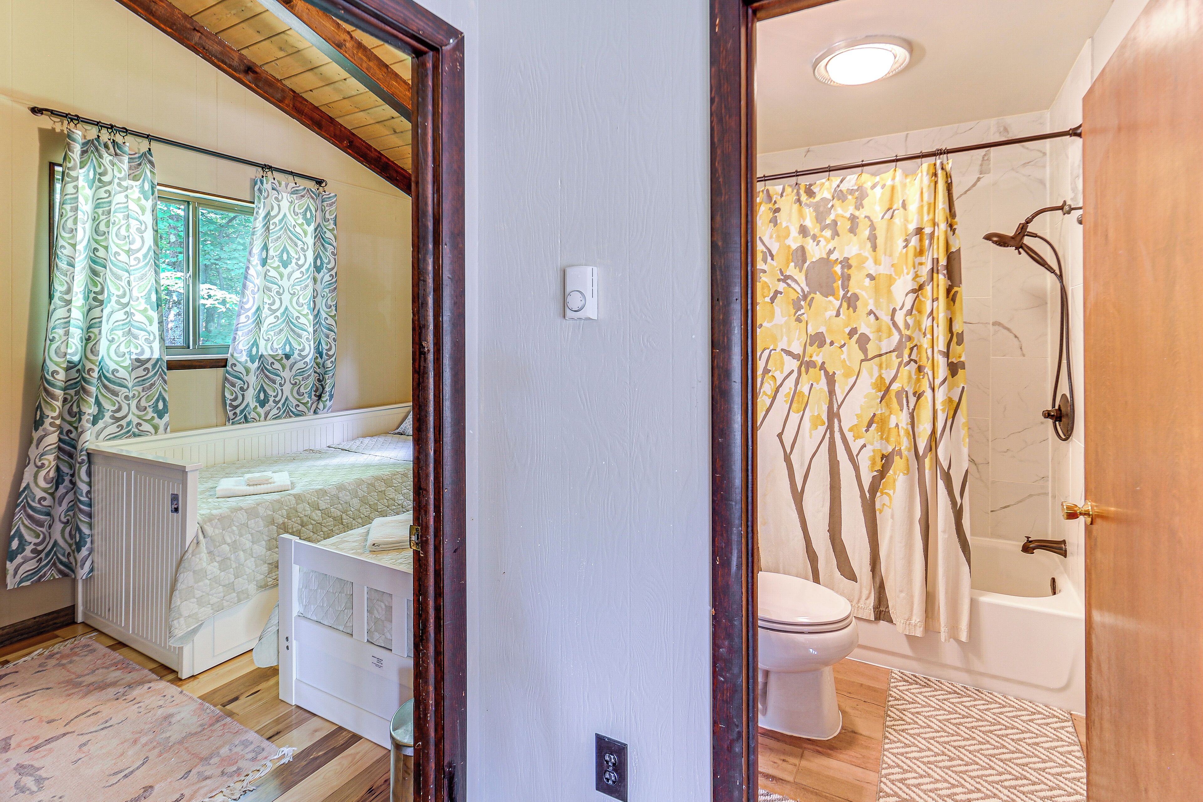 Une chambre à coucher comprenant un lit, une fenêtre avec des rideaux, un radiateur et une porte donnant sur une salle de bain équipée d’une baignoire et de toilettes.