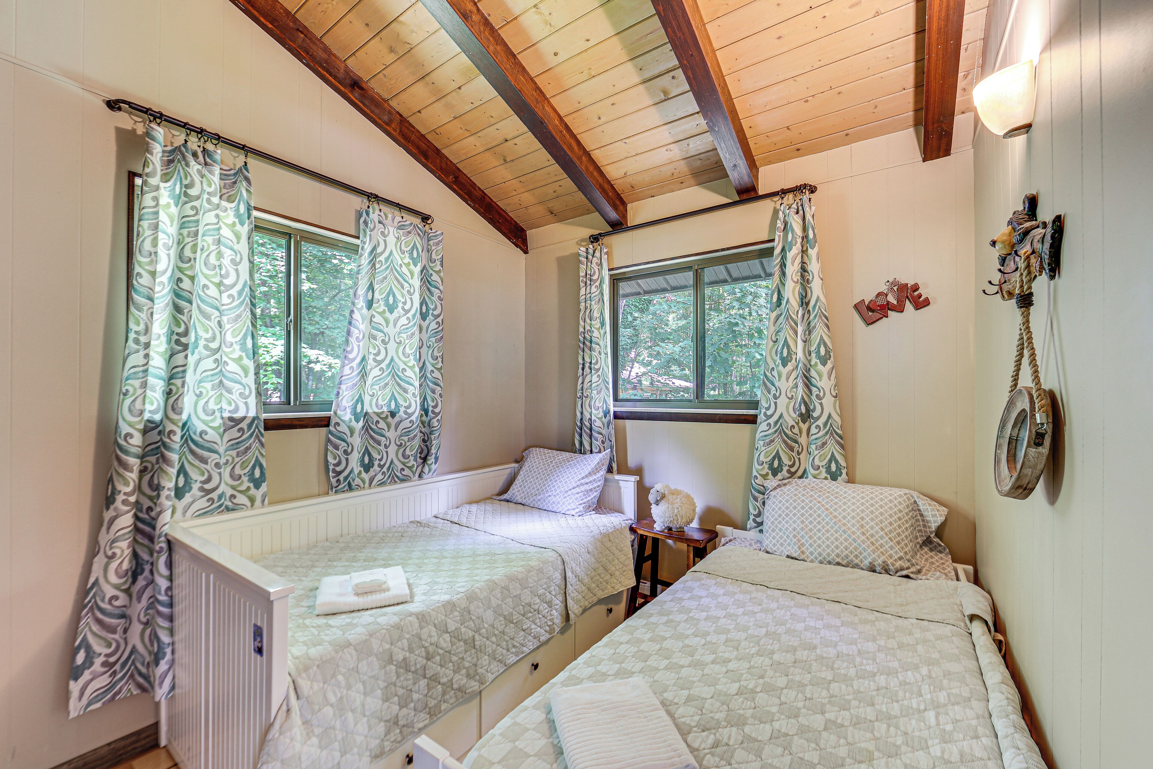 A room with two beds, a window, a radiator, and a wall-mounted lamp.