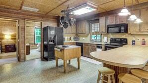 Une cuisine avec des meubles en bois, un îlot central doté de tabourets, un four à micro-ondes, une cuisinière et des ustensiles de cuisine suspendus.
