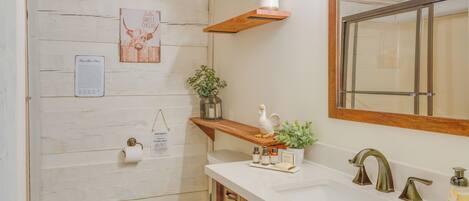 Un baño con un tocador de madera, un lavamanos blanco, un espejo y un inodoro. Hay objetos decorativos en el tocador y un calendario en la pared.