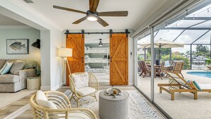 A spacious living area with a ceiling fan, wicker furniture, a round ottoman, and a view of a pool through large glass doors. - Private Fishing Dock: Waterfront Palmetto Home! (Palmetto)