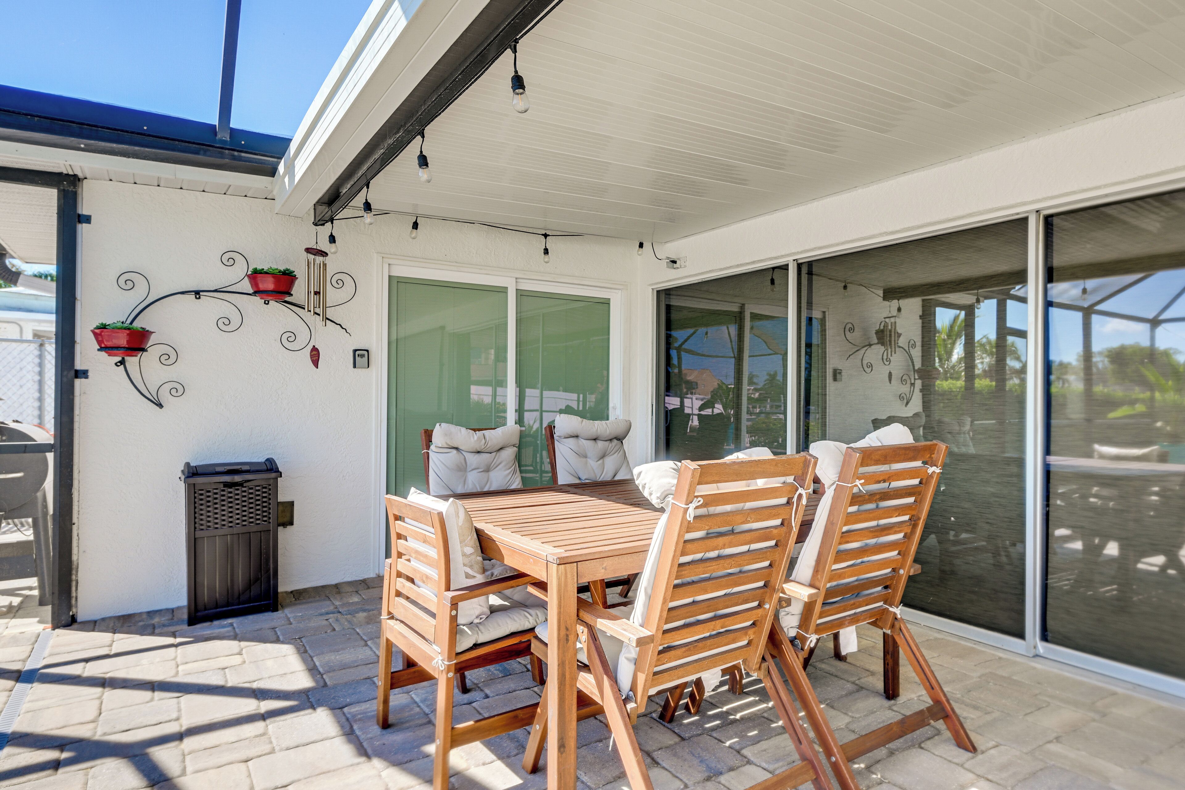 A covered patio with a wooden table and chairs, a trash bin, and decorative wall elements.