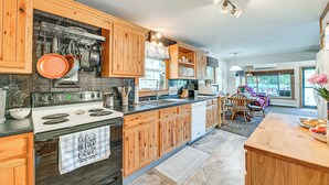 A kitchen with wooden cabinets, a stove, and a dining area with a table and chairs. - Cottage on Lamoka Lake w/ Deck, Grill & 3 Kayaks (Bradford)