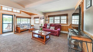 A spacious living room with a wooden coffee table, a red sofa, and a large window with blinds. - Cottage on Lamoka Lake w/ Deck, Grill & 3 Kayaks (Bradford)
