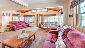 A spacious living room with a red sofa, a wooden coffee table, and a red couch. There are large windows with blinds, a wooden ceiling, and a sign on the wall. - Cottage on Lamoka Lake w/ Deck, Grill & 3 Kayaks (Bradford)