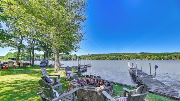 A lakeside deck with Adirondack chairs, a fire pit, and a dock extending into the water. - Cottage on Lamoka Lake w/ Deck, Grill & 3 Kayaks (Bradford)
