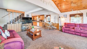 A spacious living room with a wooden ceiling, a television, a kitchen area, and a purple sofa. - Cottage on Lamoka Lake w/ Deck, Grill & 3 Kayaks (Bradford)