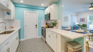 Une cuisine moderne avec des meubles blancs, un four à micro-ondes et un évier. Le sol est décoré de motifs et une porte donne accès à une autre pièce.