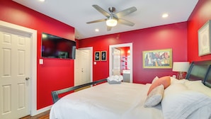 Une chambre à coucher avec un lit, un ventilateur de plafond, une télévision et un mur rouge.
