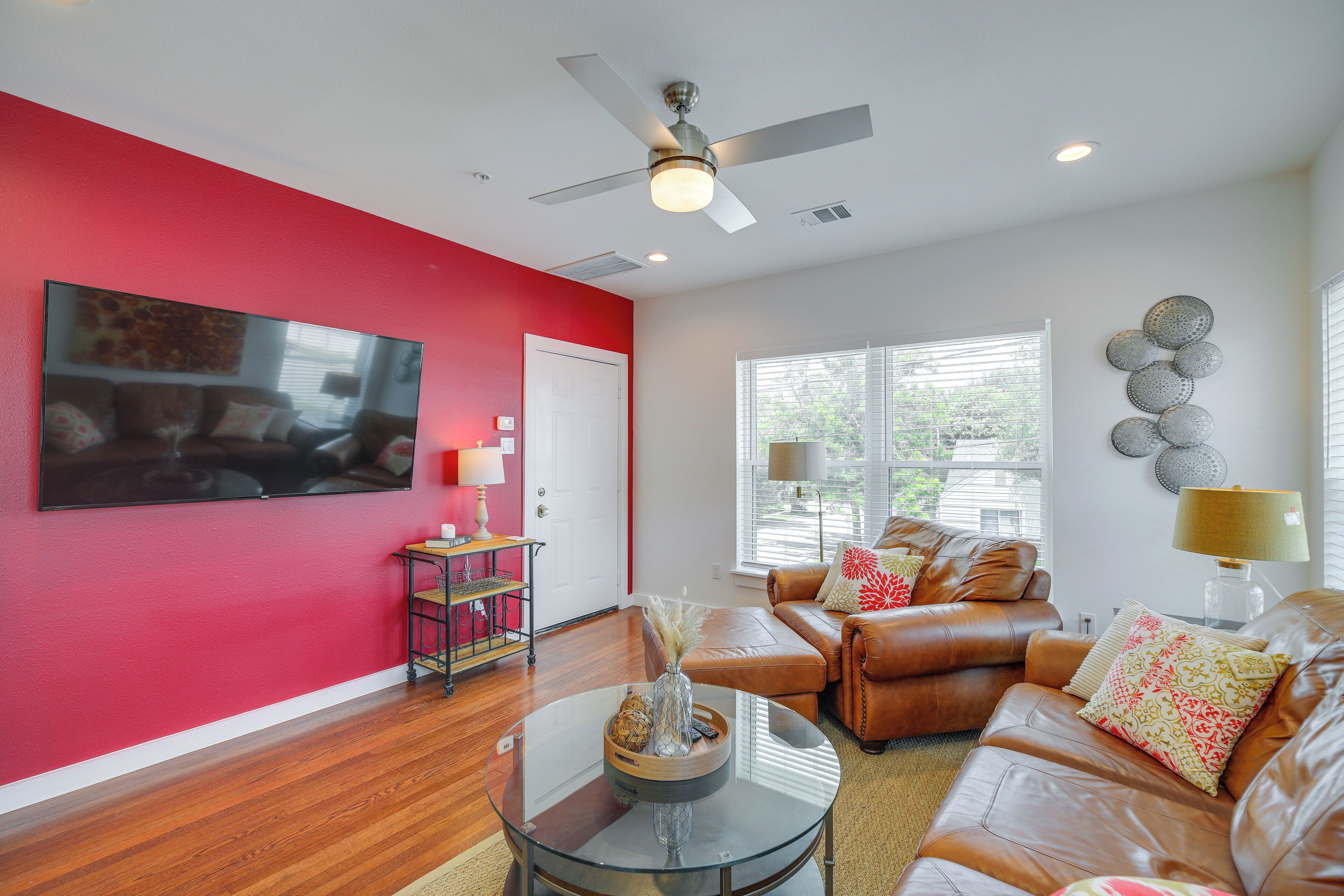 Un salon avec un mur d’accent rouge, des canapés en cuir, une table basse en verre et un ventilateur de plafond.
