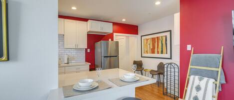 A modern kitchen with white cabinets, a stainless steel refrigerator, and a red accent wall.